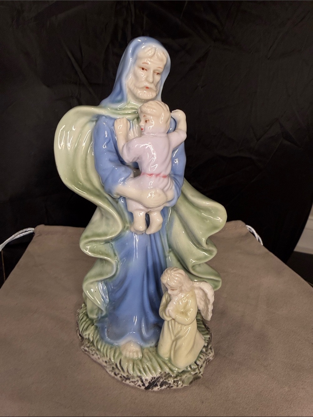 Saint Joesph holding a baby with an angel at his feet.